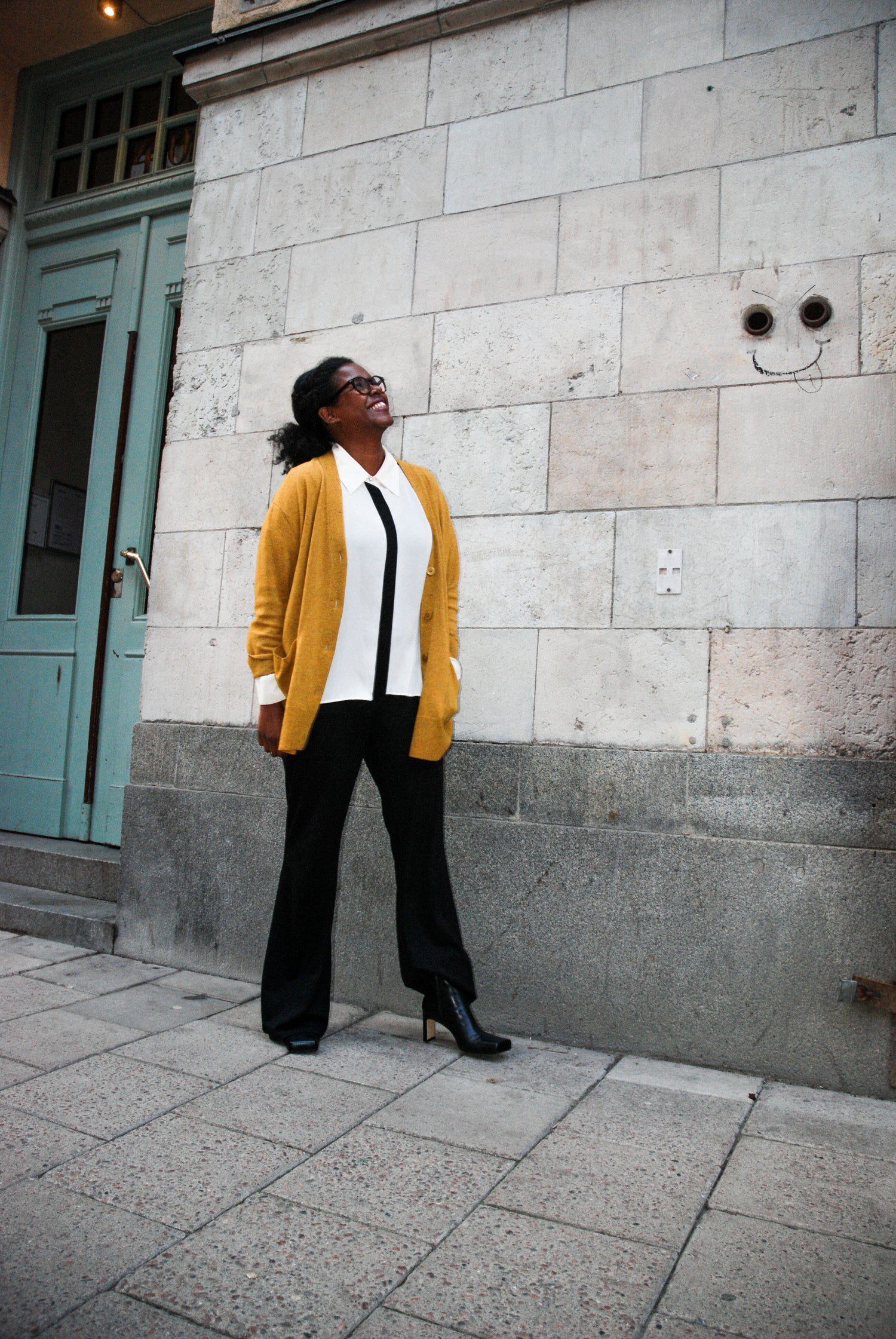 Barnbutiken Elsa & Sams ägare Johanna står och tittar uppåt mot himmelen med KINGFELT FOOTWEARs svarta skinnstövletter. Hållbart handgjorda i Italien av nappaskinn. Står vid en portuppgång vid Södermalm Stockholm mot en härlig marmorlik vägg.