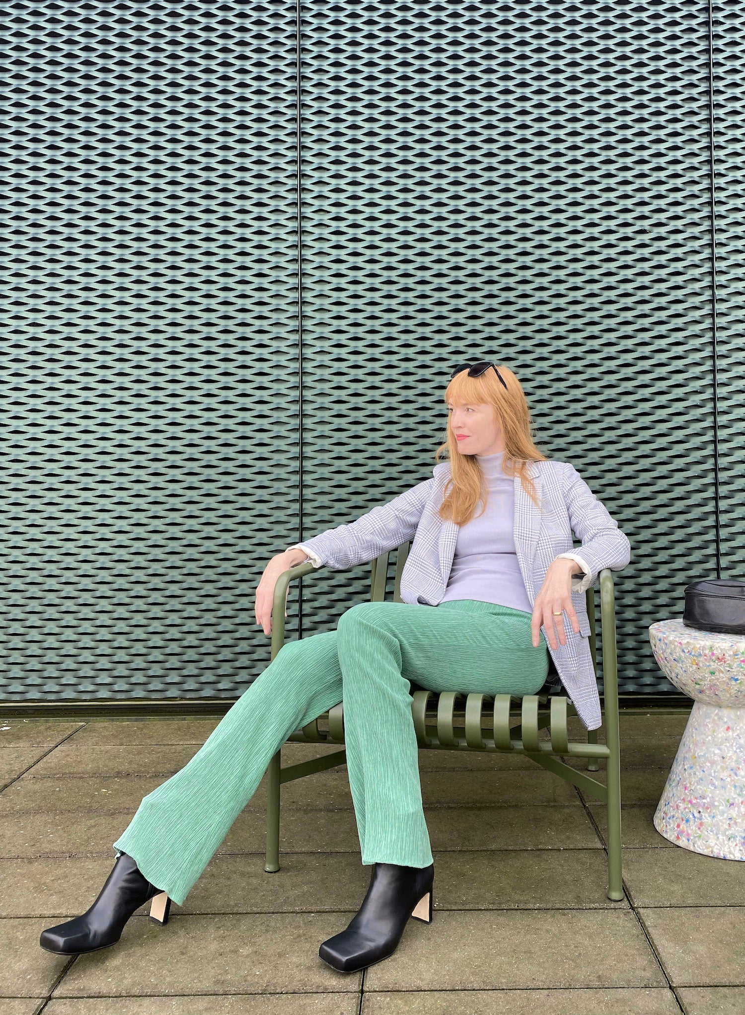 Arkitekt Rosa sitter på en grön stål stol med KINGFELT FOOTWEARs hållbara svarta skinnstövletter INGA. Handgjorda och tillverkade av mjukt nappaskinn från Italien.