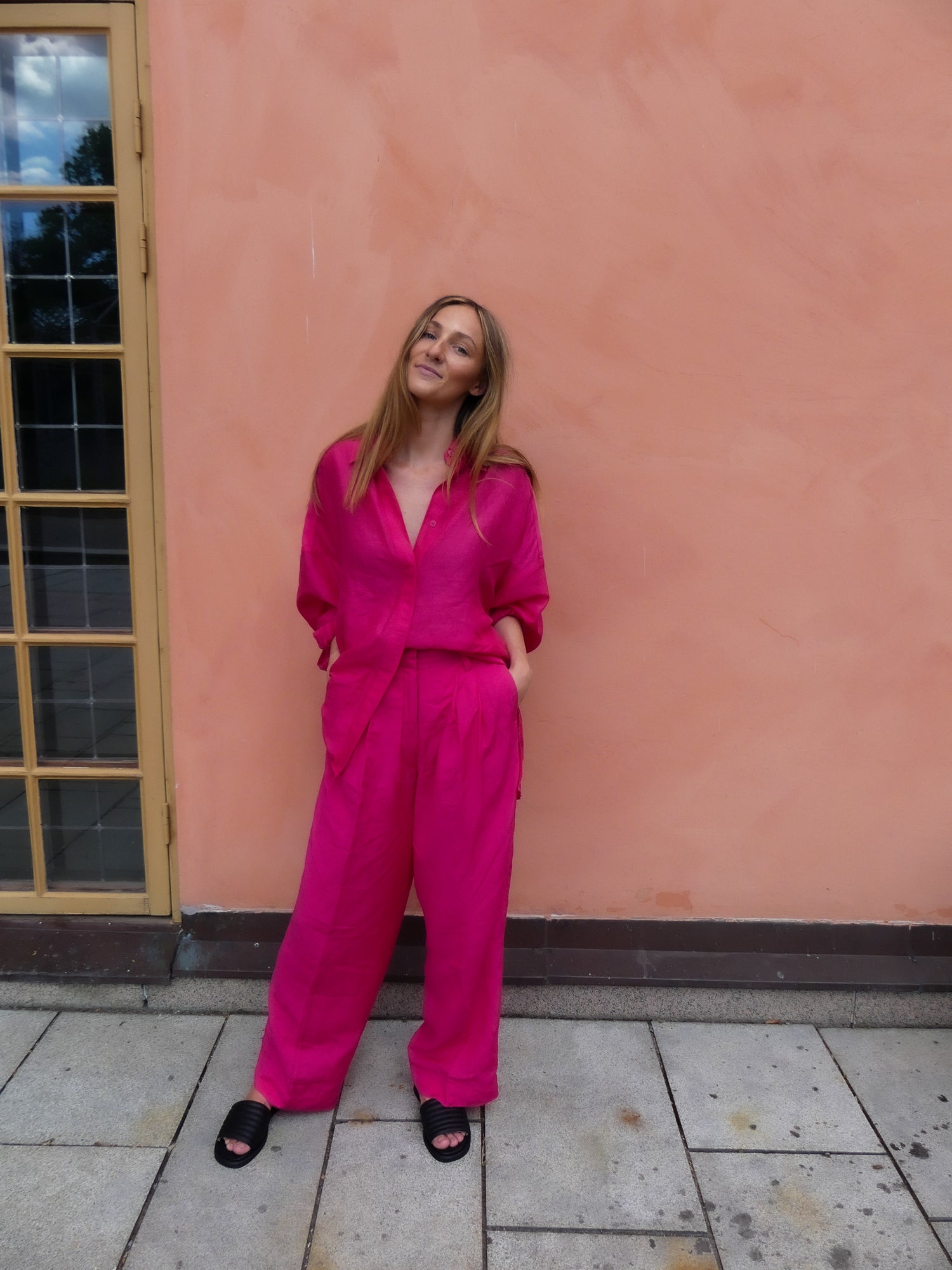 Inköparen Lisa står vid Cirkus i Stockholm i en härlig linnekostym med KINGFELT FOOTWEARs signatur sandal. Svarta slip-in sandaler av mjukt kalvskinn. Man ser ovandelen och den öppna tån och hon har händerna i fickorna.