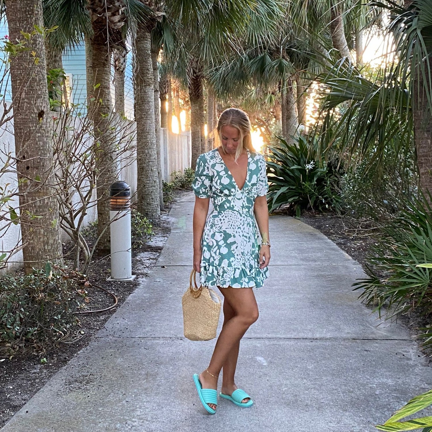 Illustratören Hanna står på en strandpromenad med KINGFELT FOOTWEARs mintgröna sklip-in sandaler i mjukt kalvskinn. Öppen tå och tillverkade i Italien.