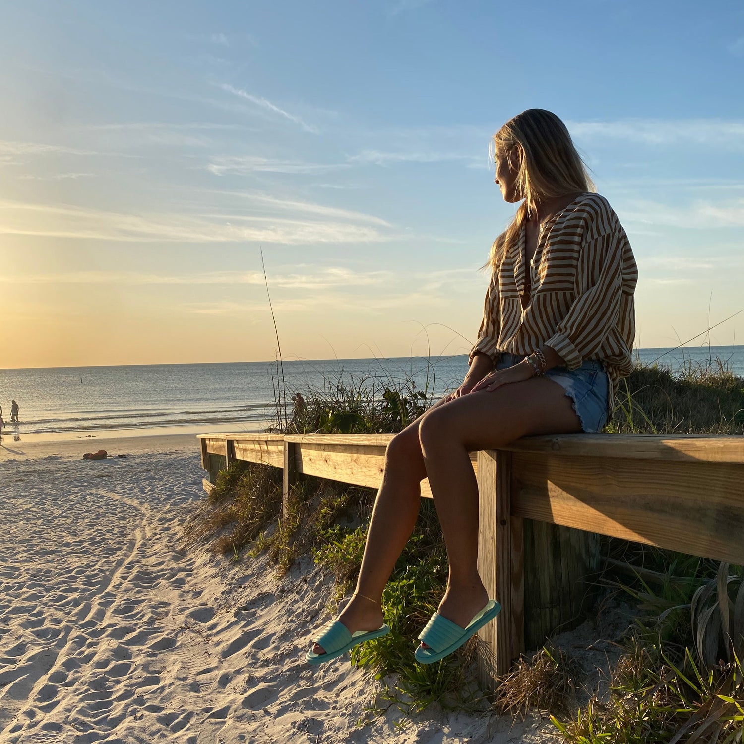 Illustratören Hanna sitter vid en pirr vid havet med ett par mintgröna slip-in sandaler med öppen tå i kalvskinn. I solnedgången vid en vacker sandstrand.