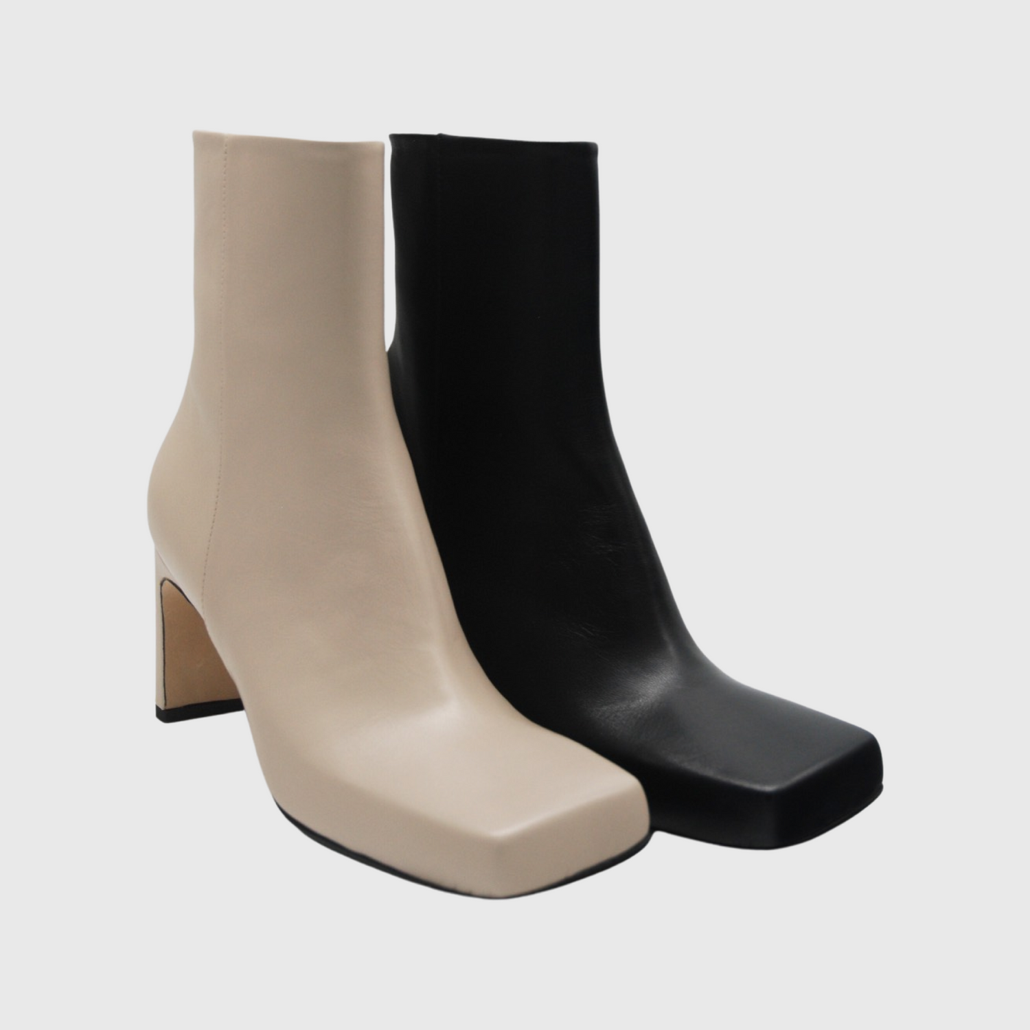 Två höger skinnstövletter i svart och beige nappaskinn. Kantig tå stövletter i skinn. Square toe ankle boots skinnstövletter i beige och svart. Ljust beige napaskinn med vero cuoio sula som skymtar vid hälen. Syns snett framifrån. Handgjorda i Italien.