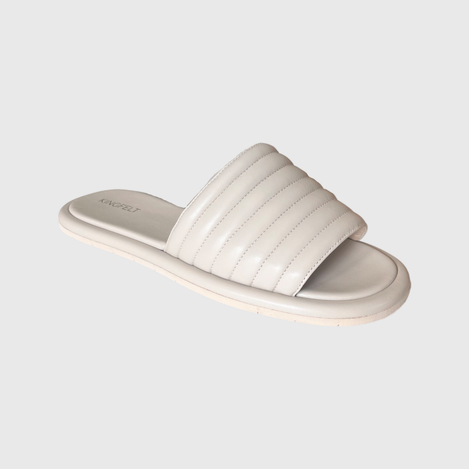 Ljus beige slip-in skinnsandal i slitstark nappaskin. Tillverkade i Italien med en öppen tå likt en hotelltoffla men i skinn. Kingfelt footwears logga synlig i guld på hälen.