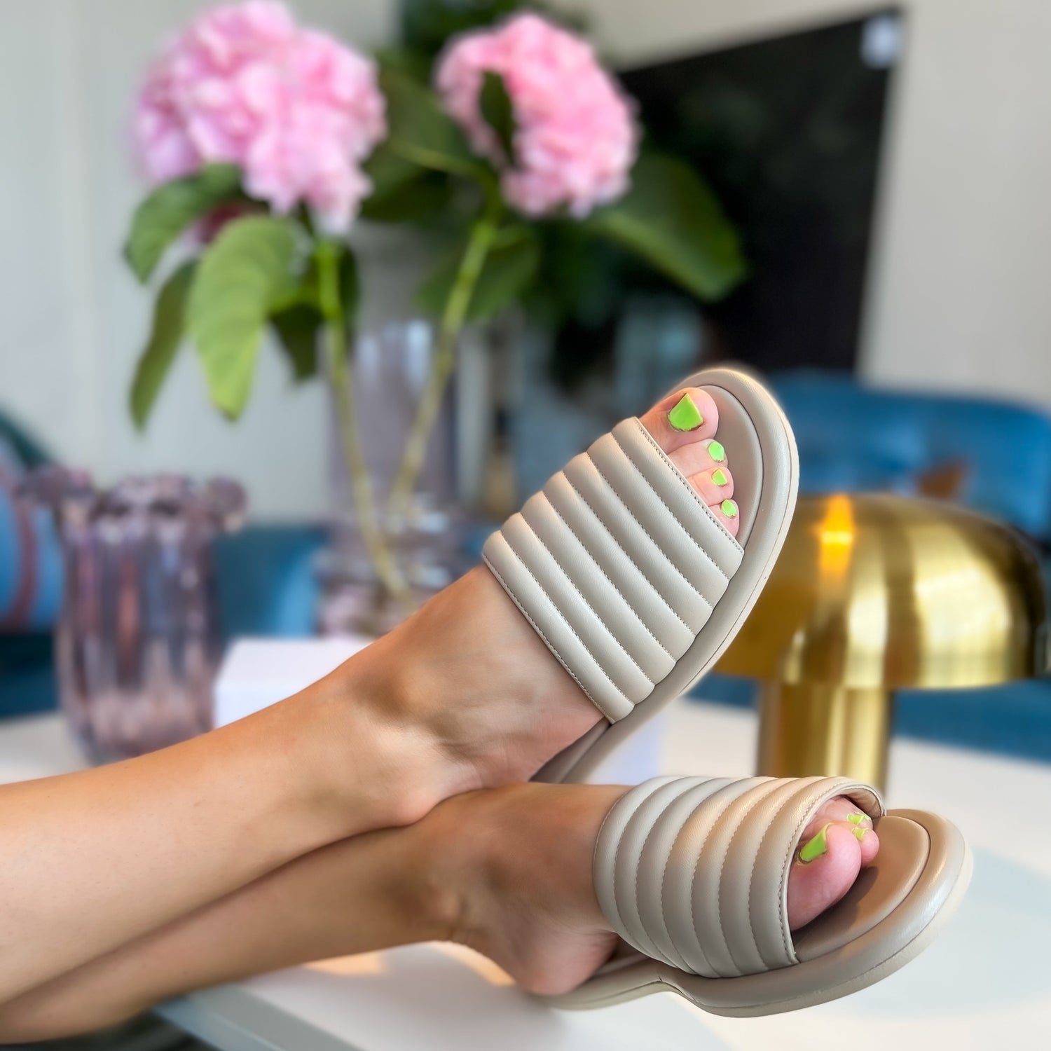 Skinnsandal i nappaskinn. Slip-in likt en hotell toffla med öppen tå och öppen häl. En ovandel av mjukt skinn och innerfoder av getskinn.Sandalerna sitter på ett par fötter som ligger pointade på ett bord. Designade av KINGFELT FOOTWEARs