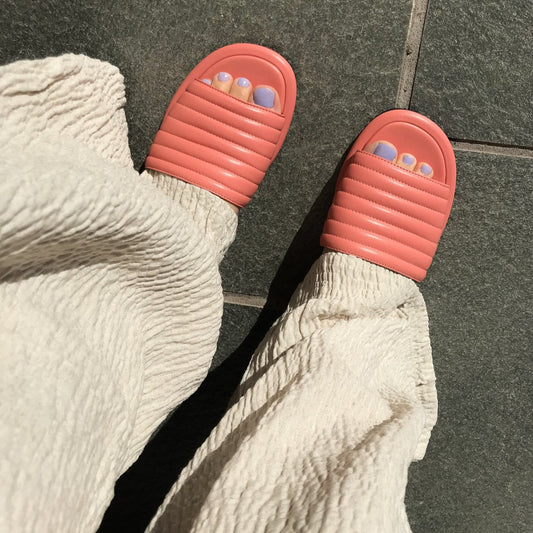 Öppen tå korallrosa slip-in sandaler i nappaskinn. Med lilla tånaglar och beige vida luftiga byxor. Ovandelen i mjukt nappa och innerfoder tillverkat av getskinn. Sommarens hetaste sandal. 